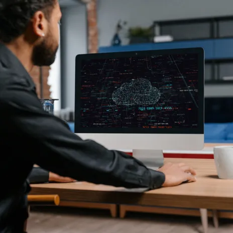 IT-Sicherheitsexperte analysiert Code auf einem Bildschirm, während im Hintergrund Kollegen über Cybersecurity-Strategien diskutieren. Mehrere Monitore mit Code- und Sicherheitsanalysen sichtbar.
