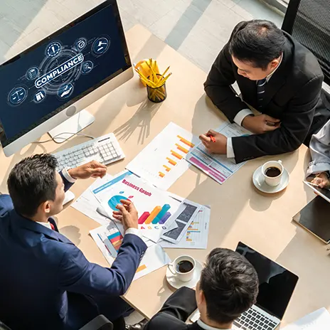IT-Sicherheitsexperte analysiert Code auf einem Bildschirm, während im Hintergrund Kollegen über Cybersecurity-Strategien diskutieren. Mehrere Monitore mit Code- und Sicherheitsanalysen sichtbar.