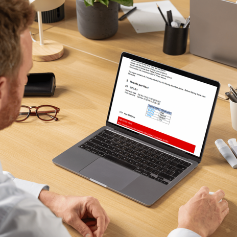 IT-Sicherheitsexperte analysiert Code auf einem Bildschirm, während im Hintergrund Kollegen über Cybersecurity-Strategien diskutieren. Mehrere Monitore mit Code- und Sicherheitsanalysen sichtbar.